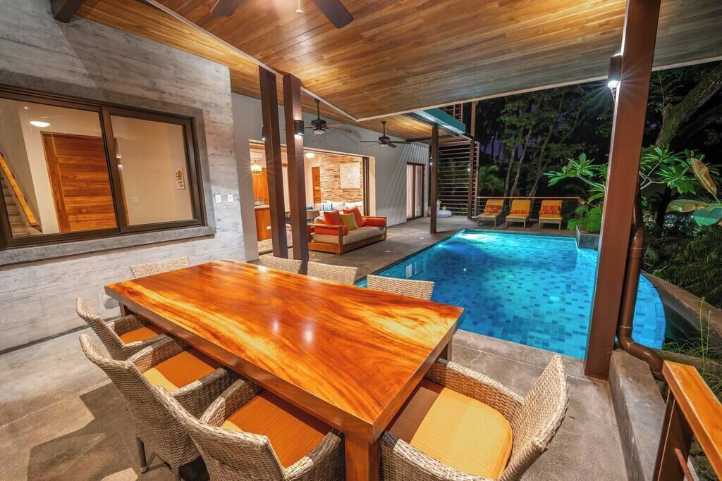 Un espace repas extérieur moderne, doté d'une piscine, de meubles en osier et offrant une vue sur la piscine.