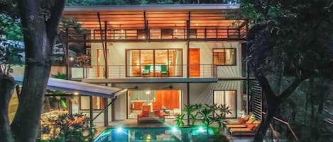 A modern two-story house with a swimming pool, surrounded by lush greenery.