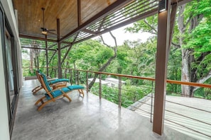 Un balcón con vista a un bosque, un ventilador de techo y dos sillones.