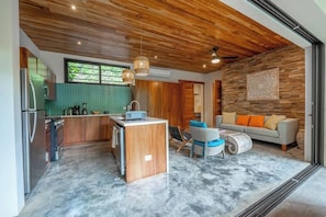 A modern kitchen with a central island, wooden ceiling, and a dining area with a sofa and chairs.