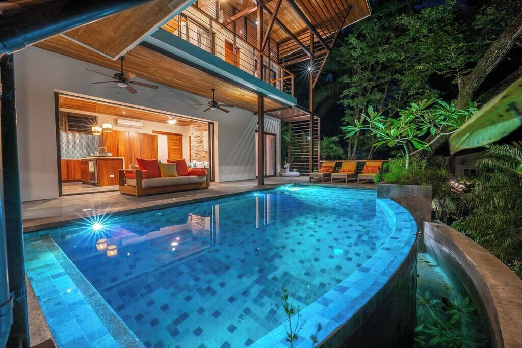 A modern pool area with a curved design, a wooden deck, and a view of the interior living space.