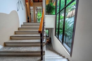 Una escalera con barandilla de madera que lleva a un rellano con amplios ventanales con vistas a la vegetación.