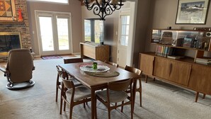 Un coin repas avec une table et des chaises en bois, un lustre et une vue sur l’extérieur par une porte.