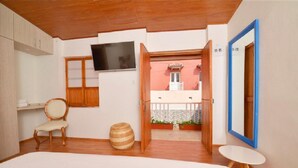 A bedroom with a bed, a chair, a television, a small table, and an open door leading to a balcony with a view of a building. - CA-4 HABITACION DOBLE EN GETSEMANI (Cartagena)