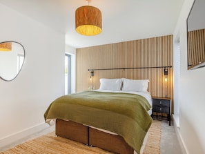 Ein modernes Schlafzimmer mit einem großen Bett, einer Wand aus Holzlamellen, einem runden Spiegel und einer Pendelleuchte.