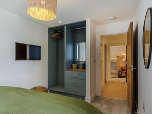 A bedroom with a bed, a wardrobe, a mirror, and a door leading to another room.