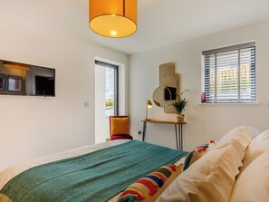 Ein modernes Schlafzimmer mit Bett, Nachttisch mit Lampe, Spiegel und Fenster mit Jalousien.