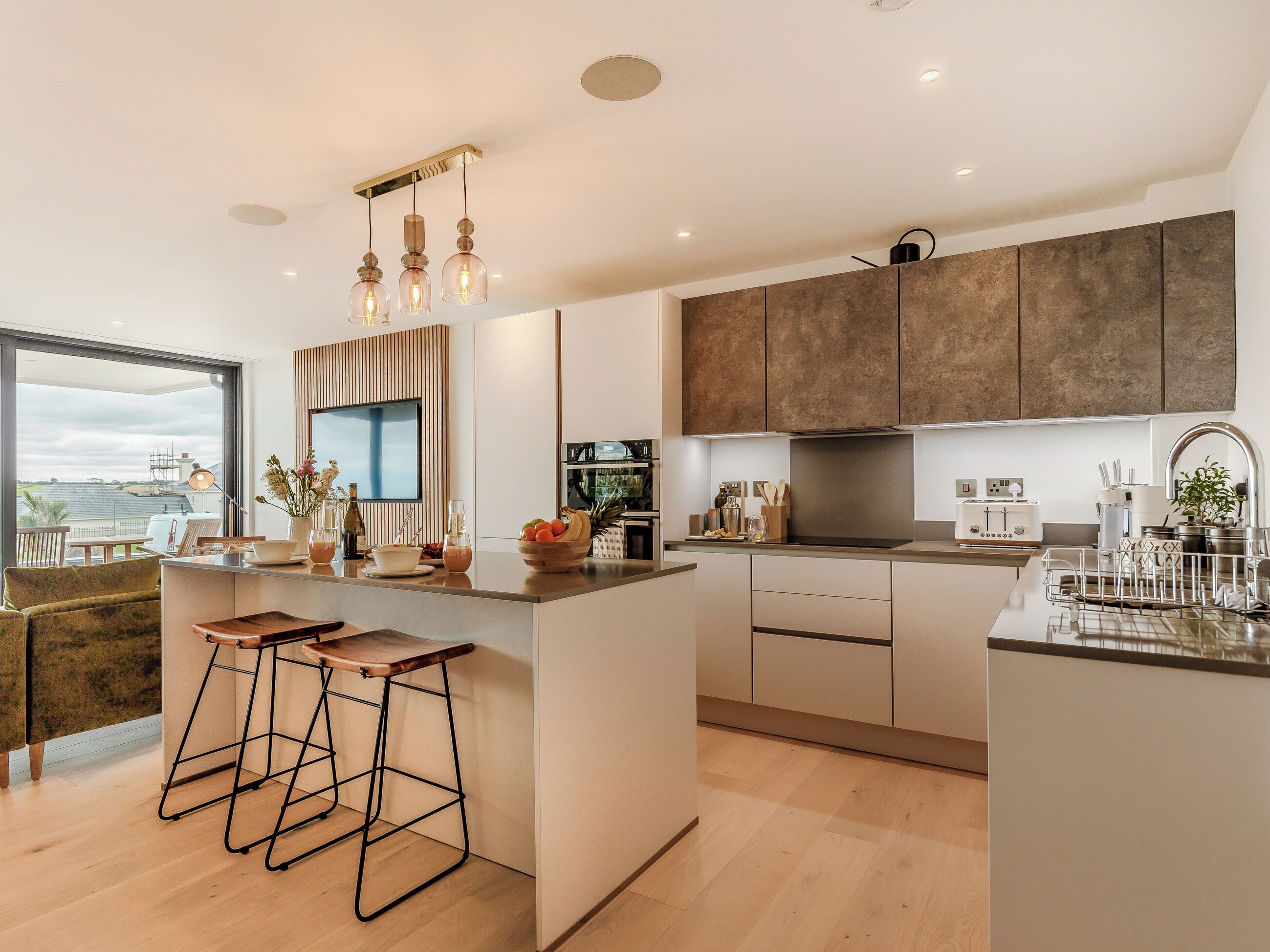 A modern kitchen with a large island, bar stools, a built-in oven, and a large window offering a view.