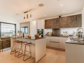 A modern kitchen with a large island, bar stools, a built-in oven, and a large window offering a view.