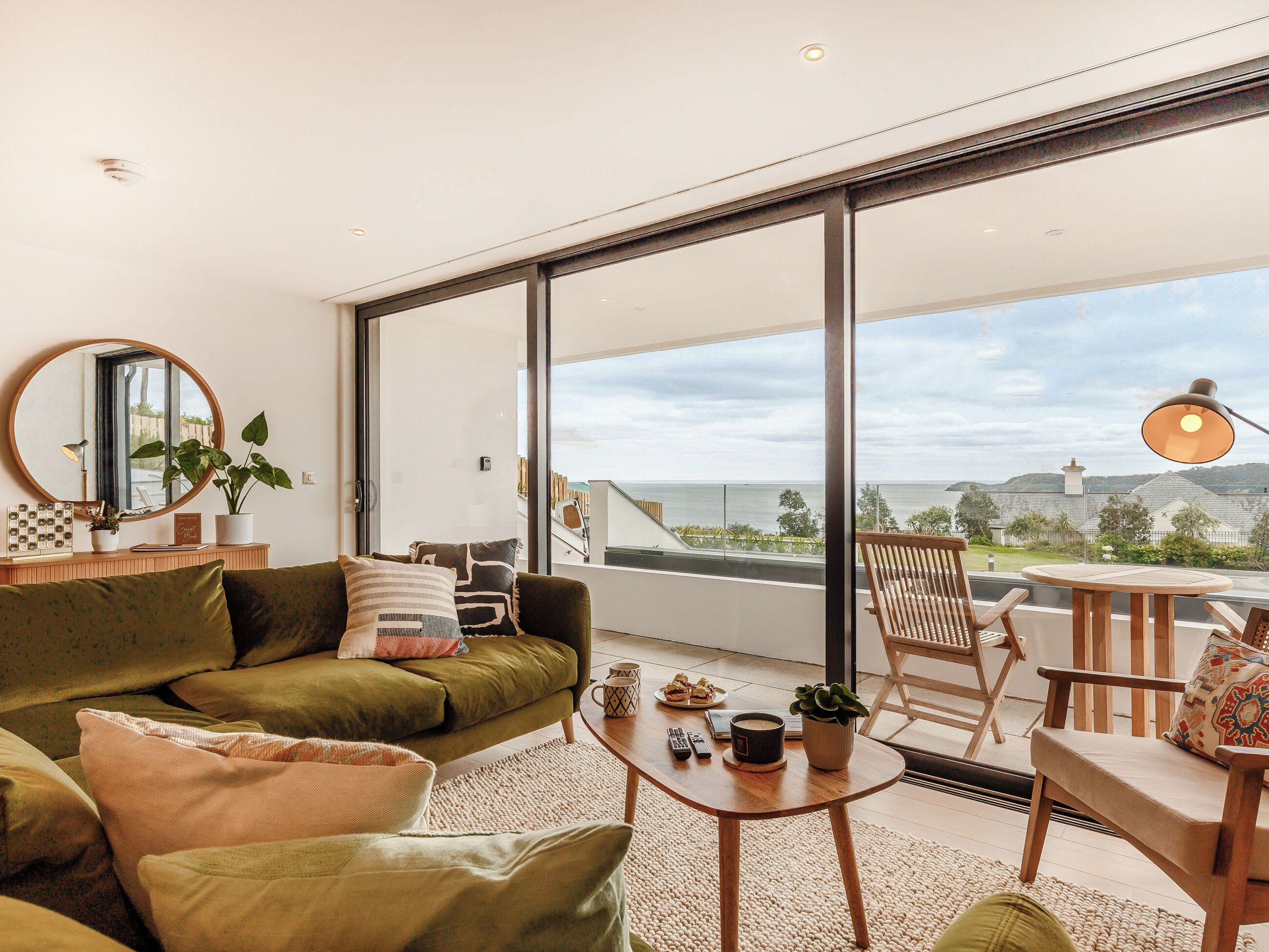 A modern living room with a green sofa, a round coffee table, and a view of the sea through large windows.