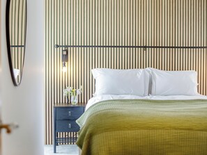 A neatly made bed with white linens, a bedside table with a vase of flowers, and a wall-mounted light fixture.