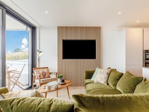 Ein modernes Wohnzimmer mit einem grünen Sofa, einem Holztisch und einem an einer Holzvertaufassung befestigten Fernseher.