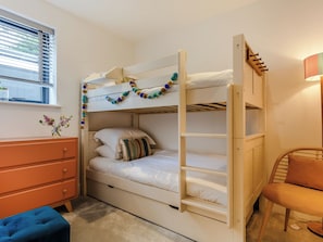 Un lit superposé avec une échelle, une commode, une chaise et une fenêtre avec des stores.