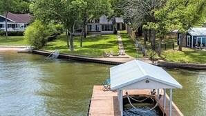 Un muelle con una estructura cubierta, un pequeño bote y una zona verde con árboles.