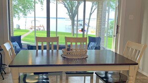 Comedor con una mesa grande, sillas y vistas a un lago a través de puertas de vidrio.