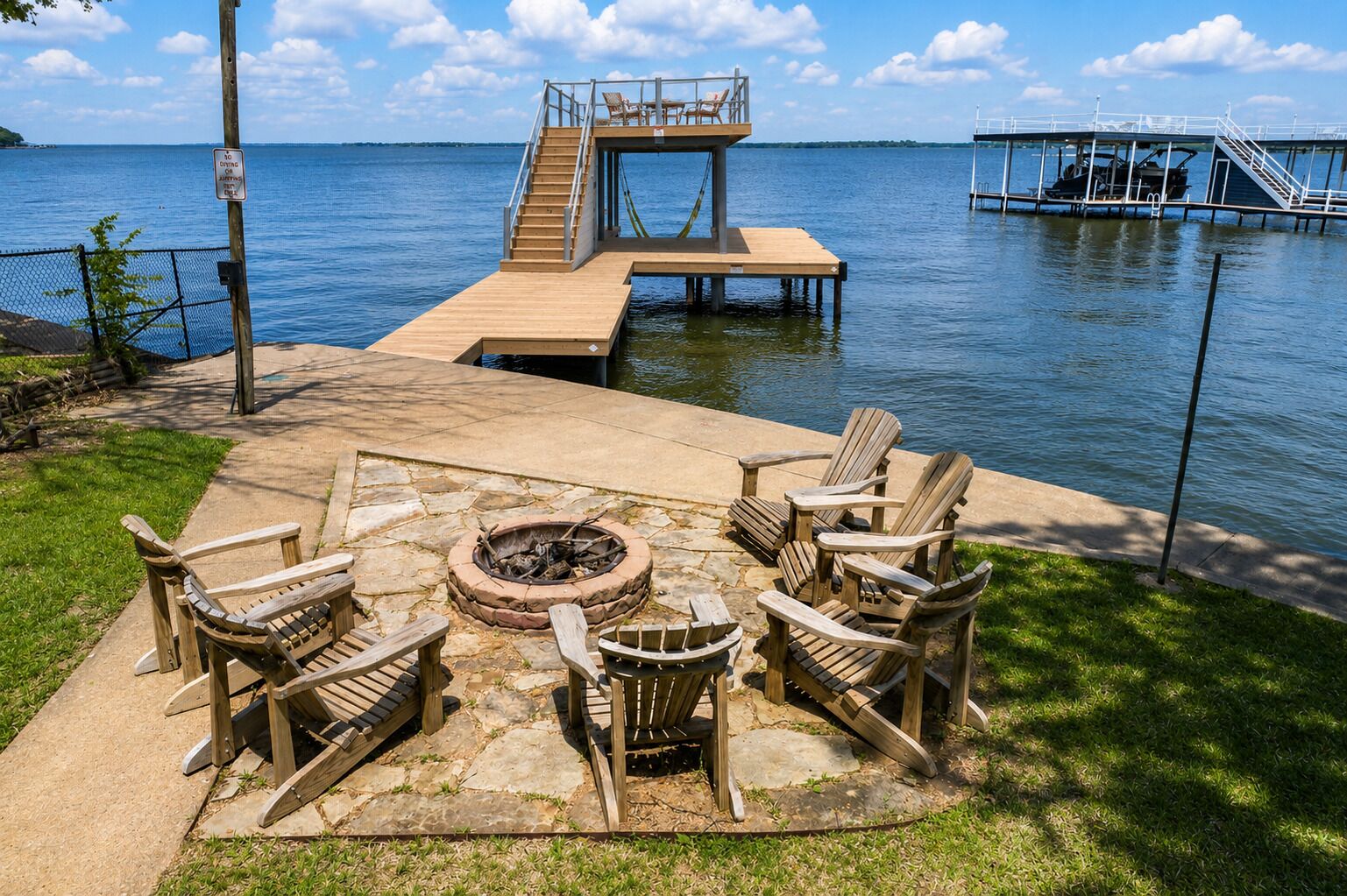 Eine Holzterrasse mit Adirondack-Stühlen, einer Feuerstelle und einem Steg, der sich in einen See erstreckt.