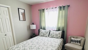Quarto com cama, cadeira, mesa de cabeceira, luminária e ventilador de teto.
