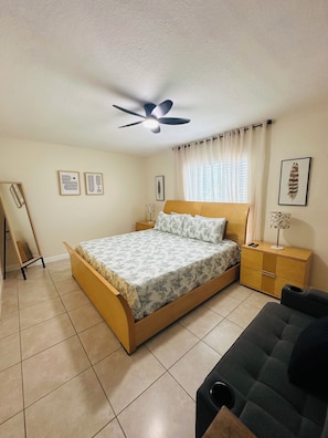 A bedroom with a bed, a ceiling fan, a bedside table, a nightstand, a lamp, a dresser, and a chair.