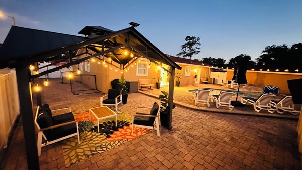 An outdoor patio area with a covered seating area, a pool, and lounge chairs.