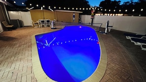 A swimming pool with a curved edge and a brick patio surrounding it.