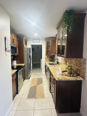 A kitchen with wooden cabinets, a granite countertop, a refrigerator, and a microwave.