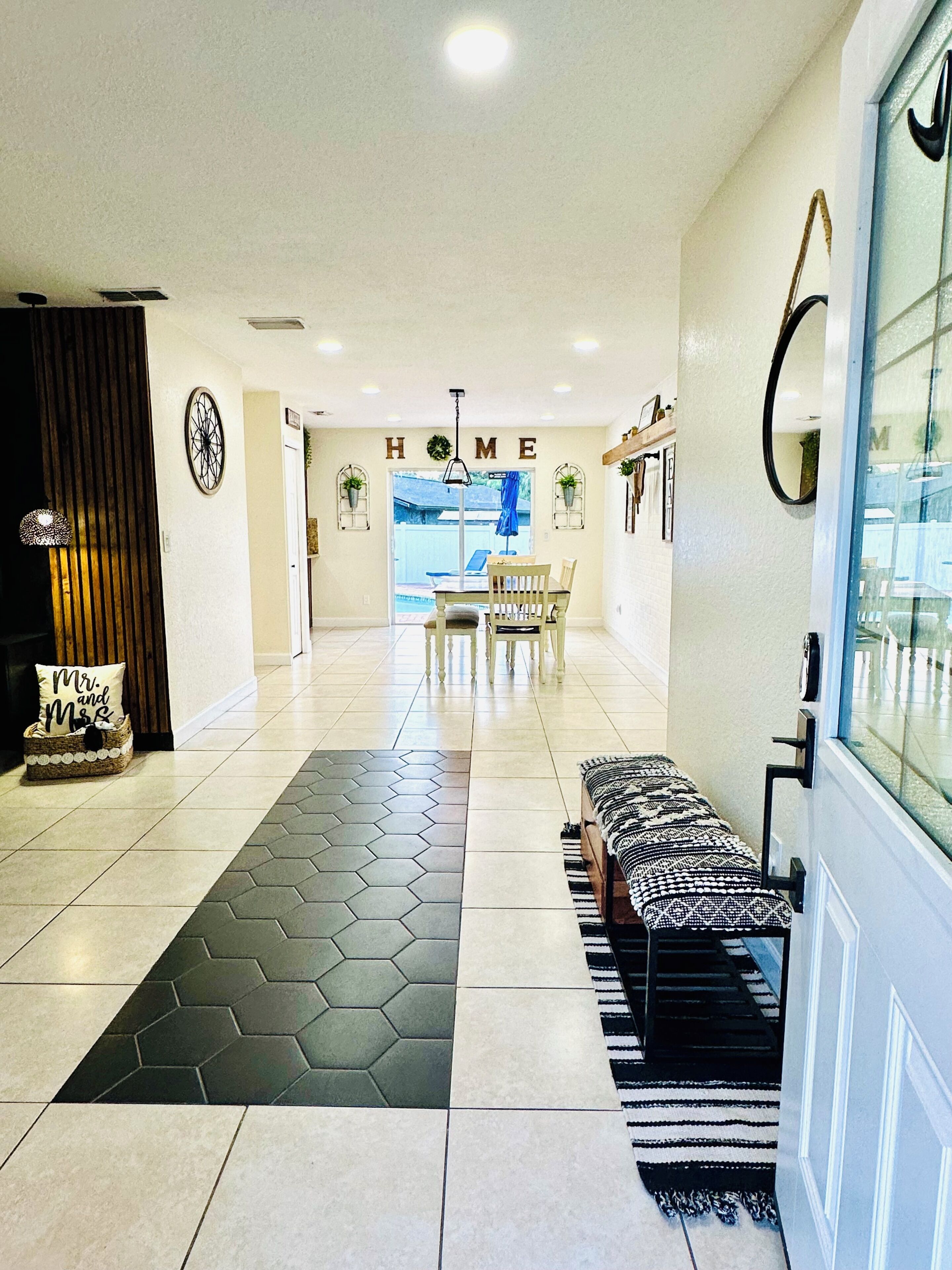 A modern interior with a hexagonal patterned rug, a bench, and a 'HOME' sign above a doorway leading to a dining area.