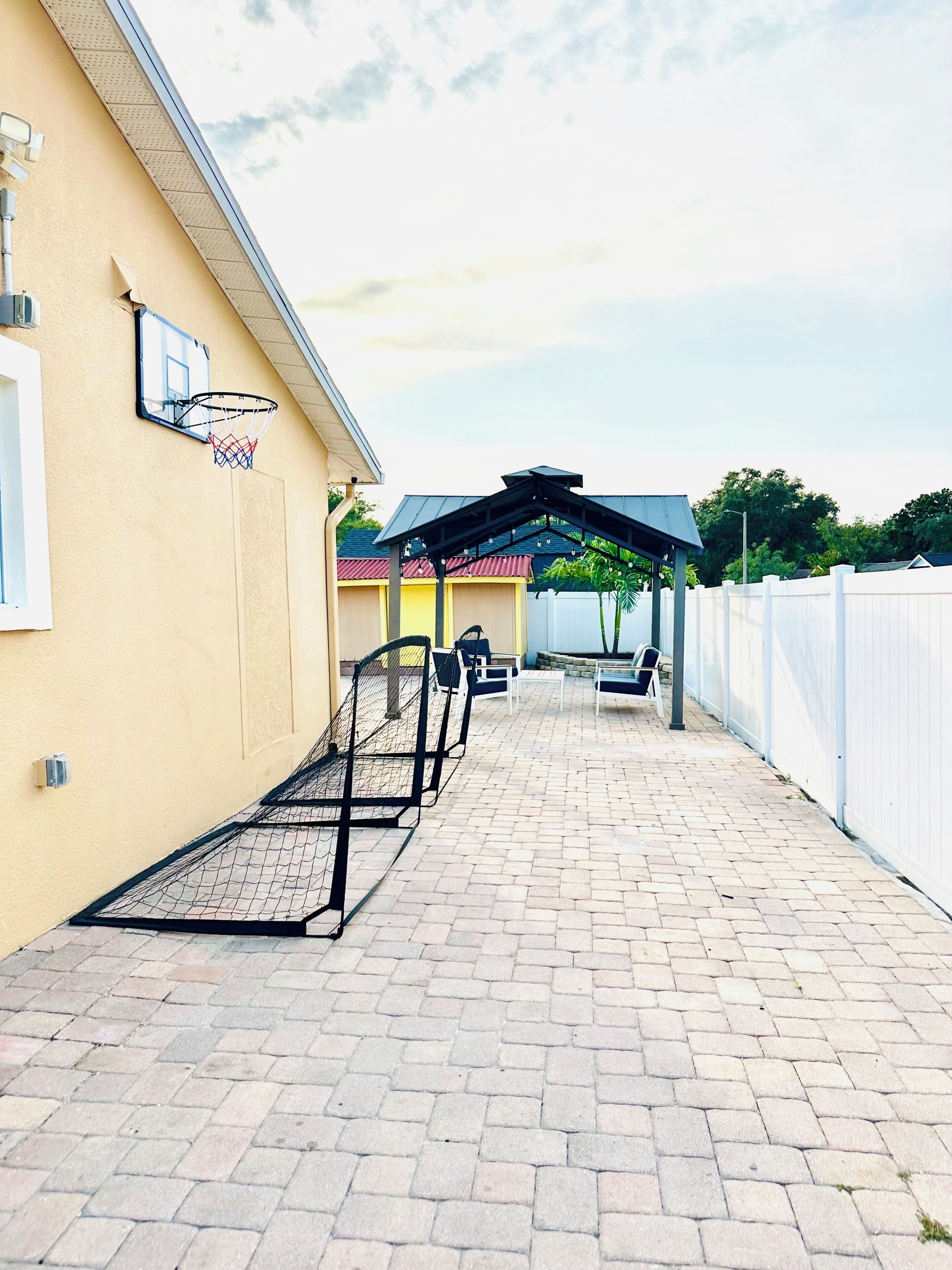 A paved walkway leading to a covered seating area with a basketball hoop on the side.