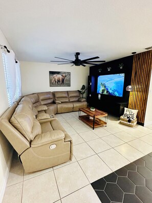 Ein Wohnzimmer mit Ecksofa, Flachbildfernseher, Deckenventilator und Wanddekoration.