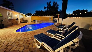 A swimming pool with lounge chairs and a brick patio.