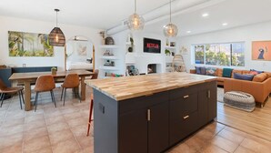 Una cocina moderna con una isla central, un comedor con sillas, un sofá y un televisor montado en la pared.