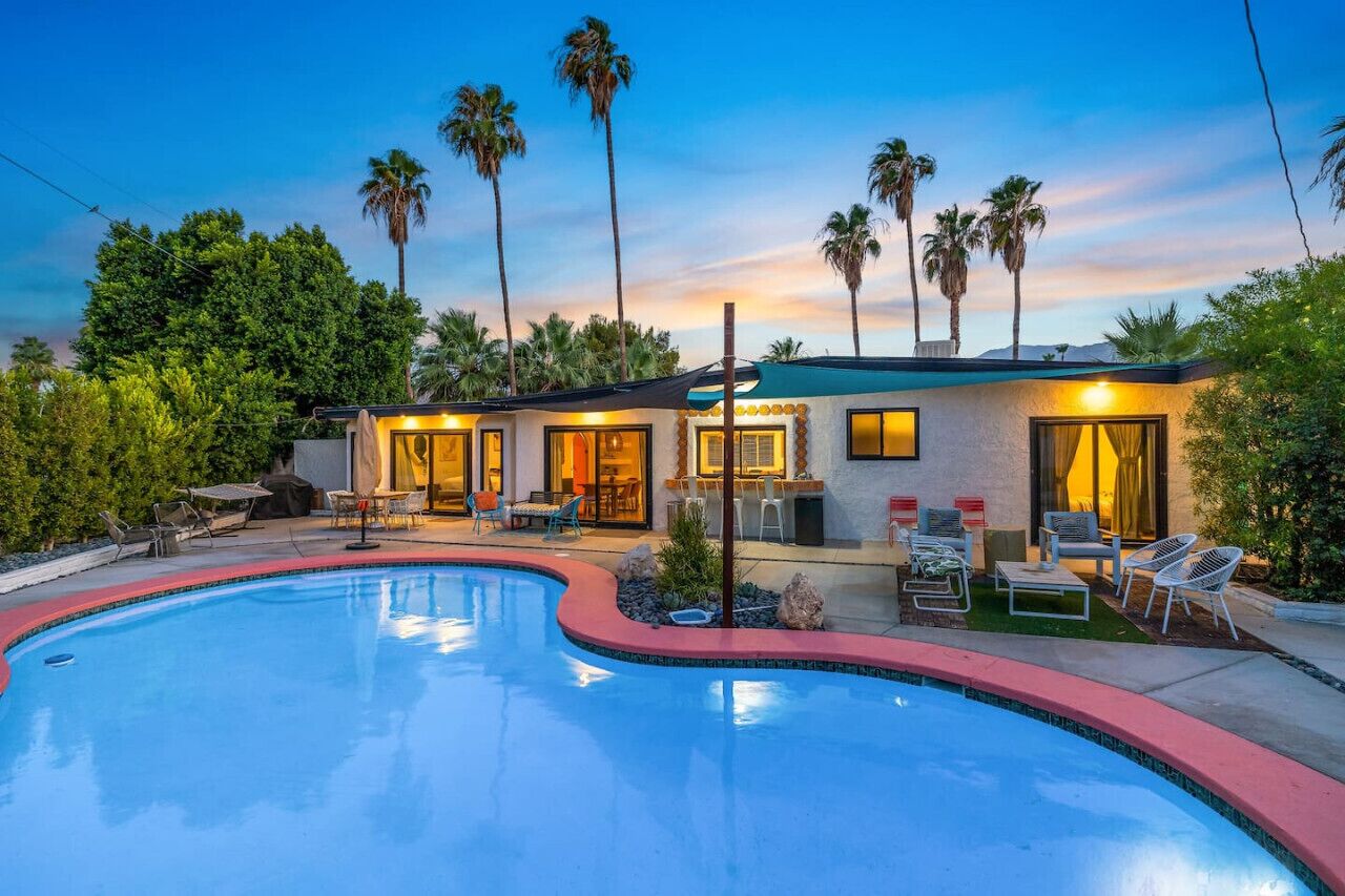 Una casa moderna con piscina, mobiliario exterior y palmeras.