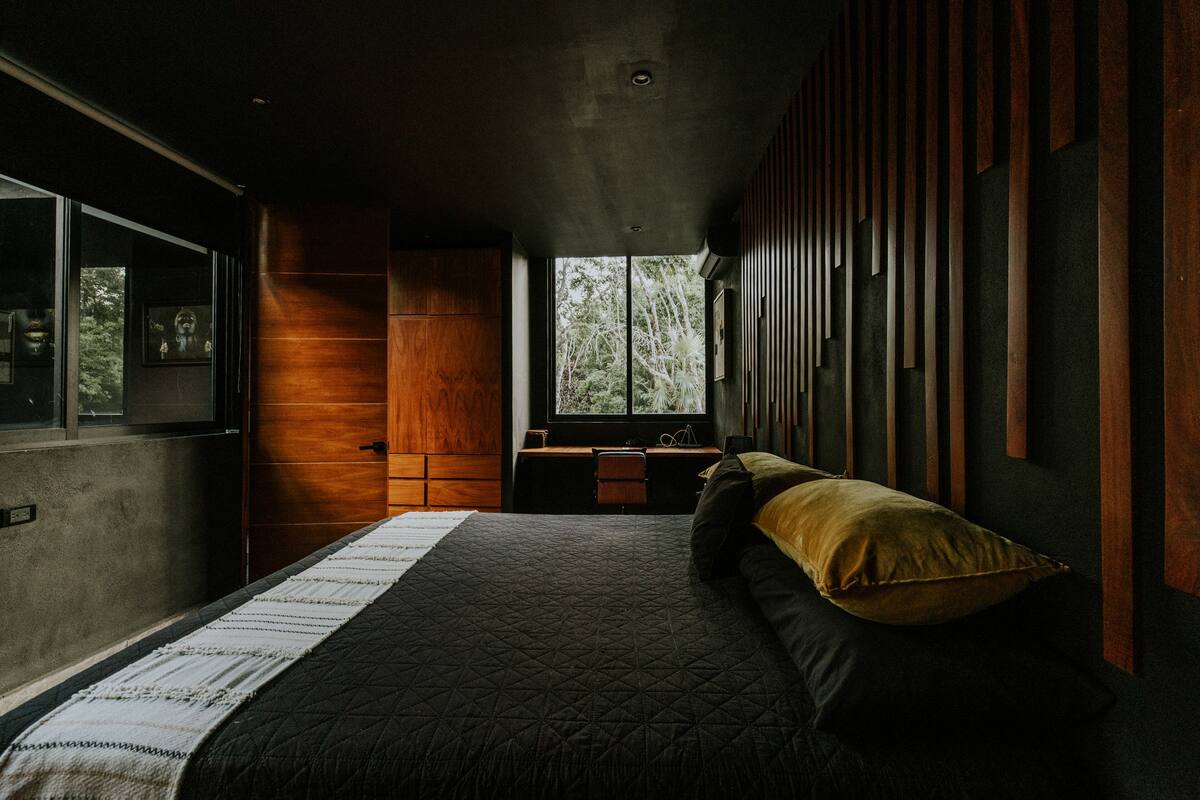 A modern bedroom with a large bed, a desk, and a window with a view of trees.