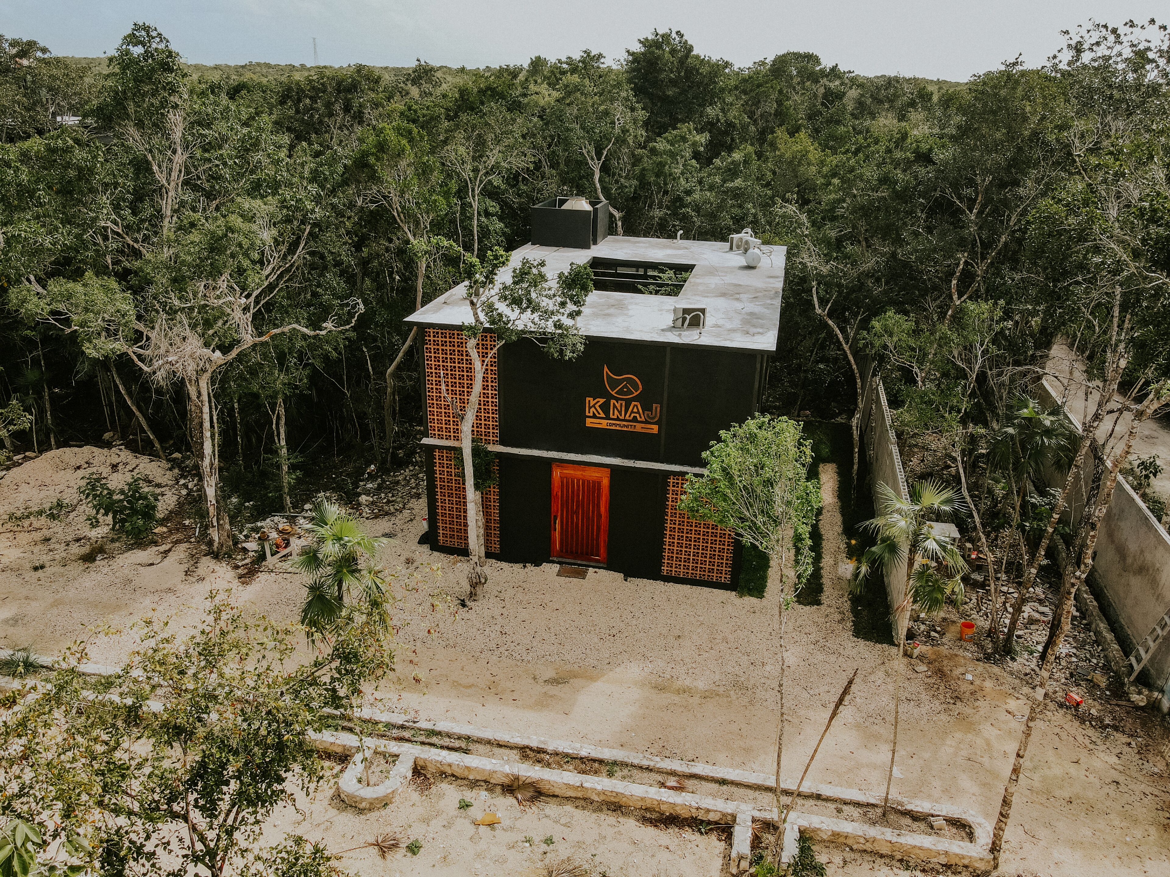 A two-story building with a black facade and orange accents, surrounded by dense greenery.