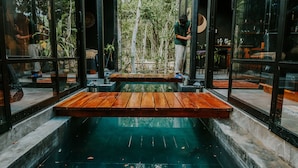 Un intérieur moderne agrémenté d’un élément aquatique central, de bancs en bois et de murs en verre offrant une vue sur l’extérieur.