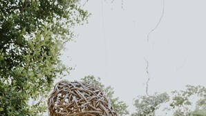 Une sculpture en osier, intégrée dans un environnement naturel, avec un sentier en pierre et un bassin d’eau claire.