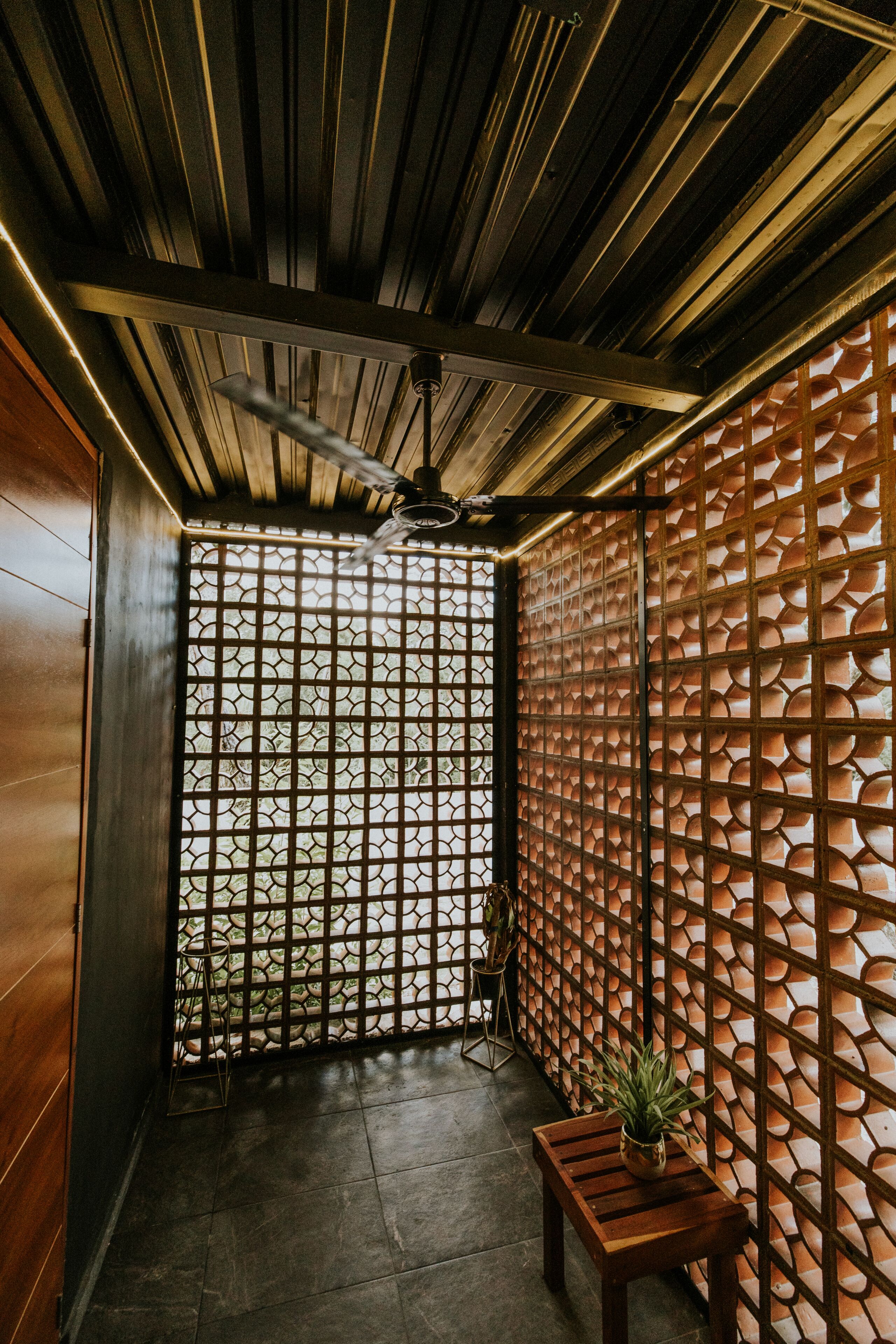 A corridor with a ceiling fan, a wooden bench, and a wall with a geometric pattern.
