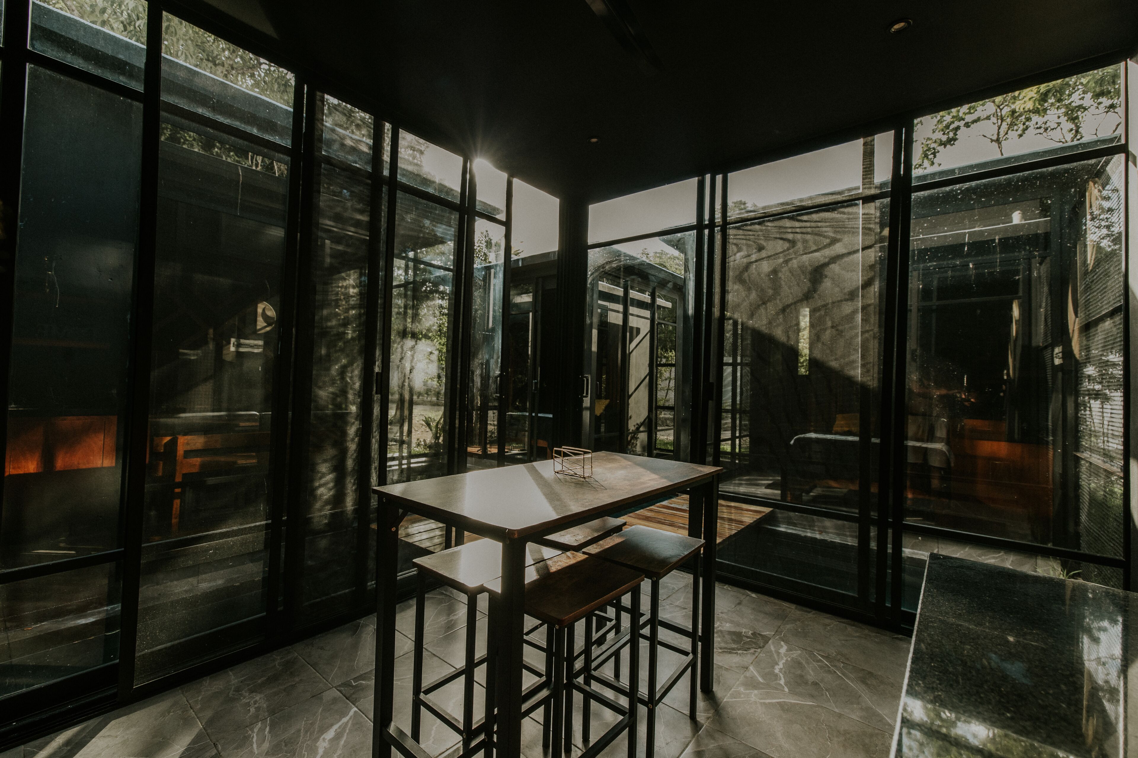 A modern interior with a large table and bench, large windows, and a view of the outdoors.