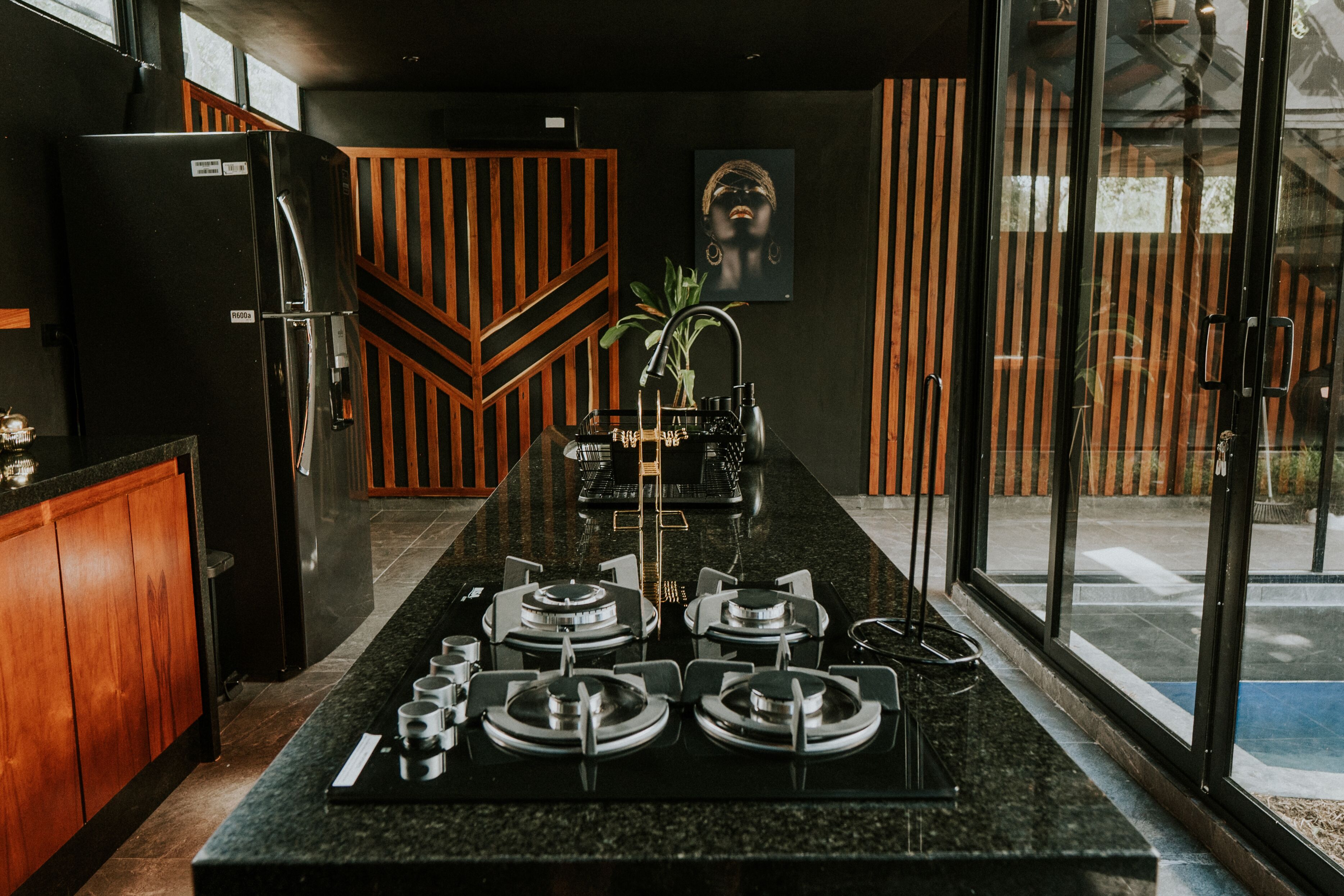A modern kitchen with a central island, wooden accents, and a large window.