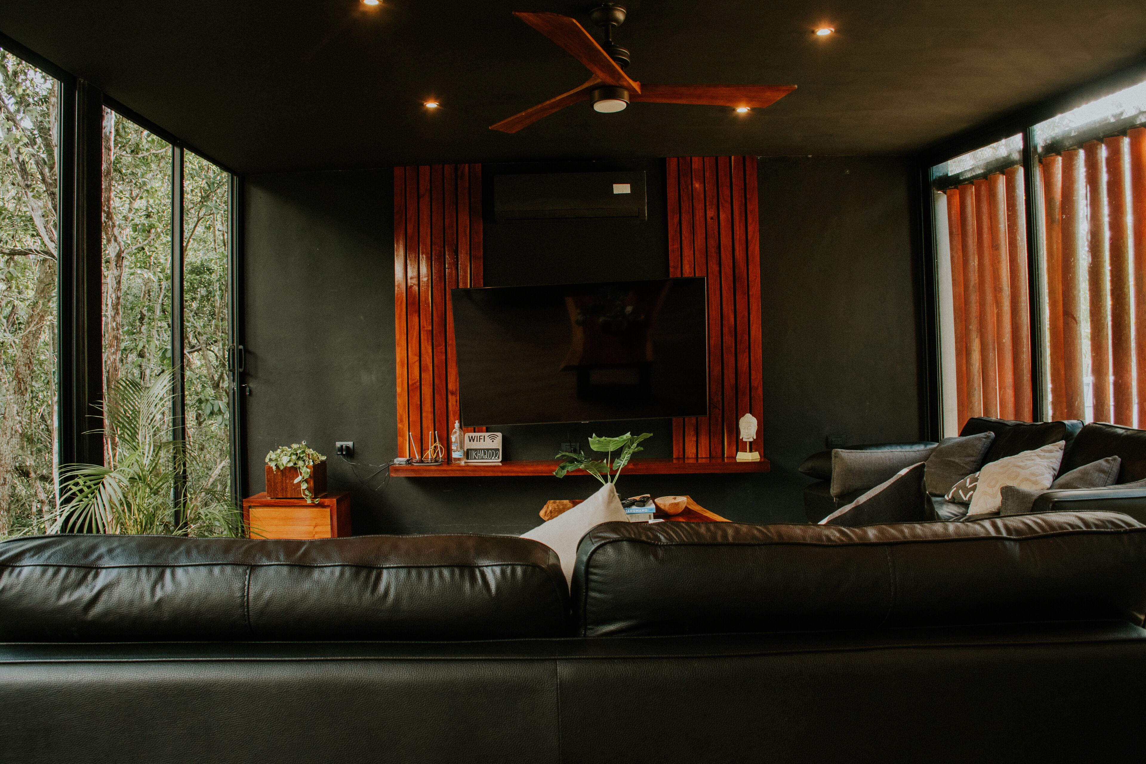 Een moderne woonkamer met een zwarte leren bank, een flatscreen televisie aan de muur en een plafondventilator.
