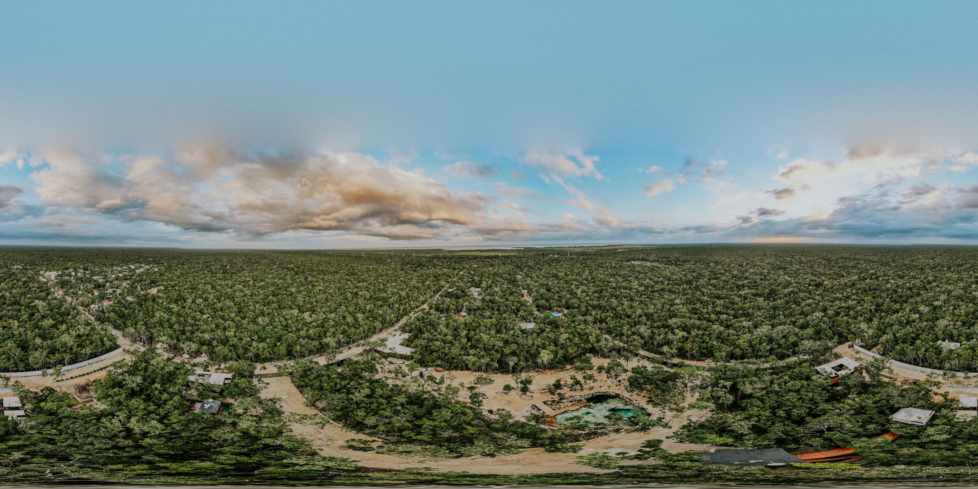 A panoramic view of a forested area with scattered buildings and a clear sky.