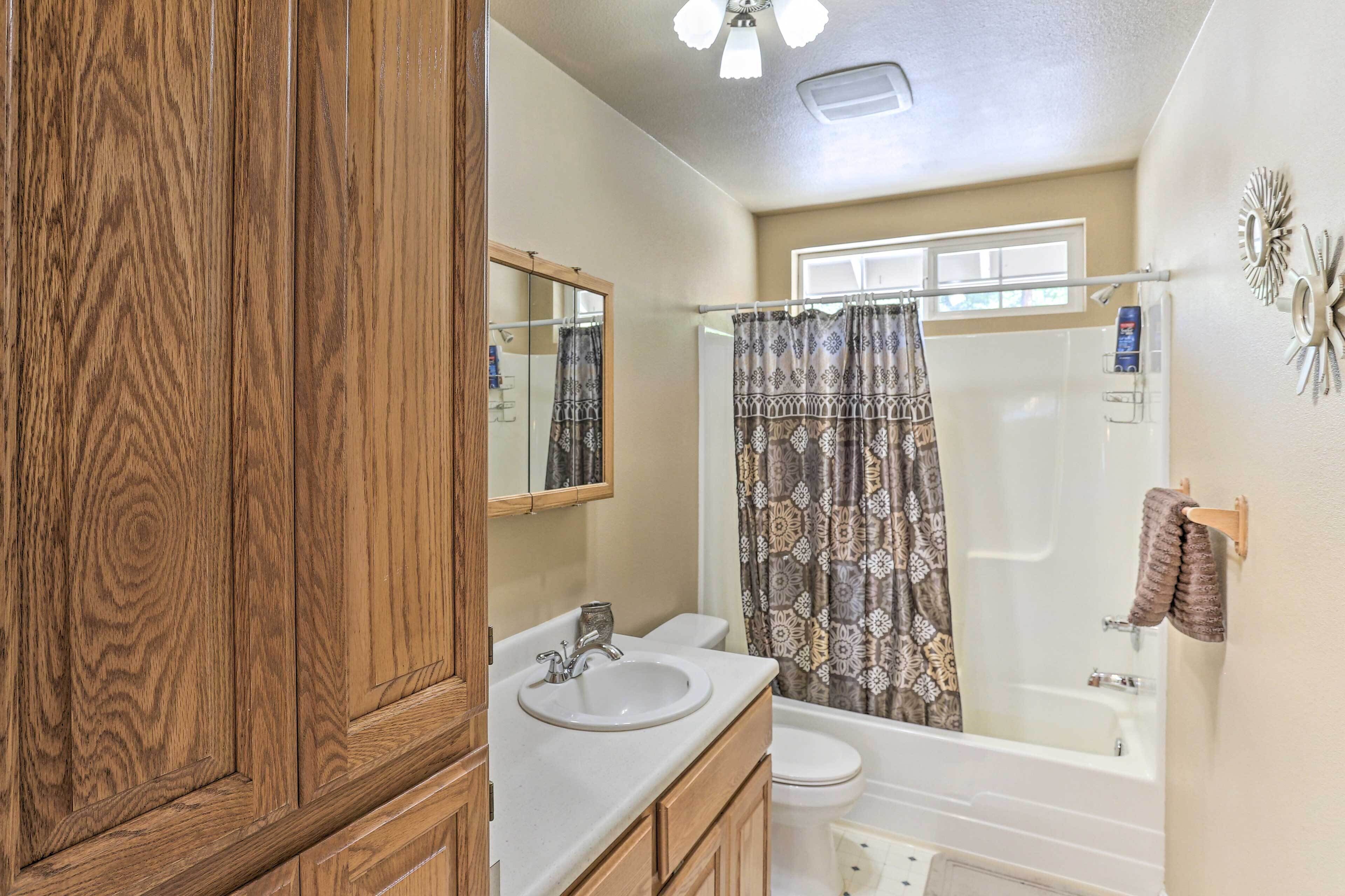 Une salle de bain avec un meuble-lavabo en bois, deux vasques, des toilettes et une douche agrémentée de rideaux à motifs.