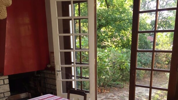 Een eetruimte met een tafel gedekt voor twee personen, een rode bakstenen open haard en uitzicht op een tuin door een glazen deur.