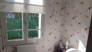 Een slaapkamer met een groot bed, een raam met uitzicht op groen, een radiator en behang met een patroon.