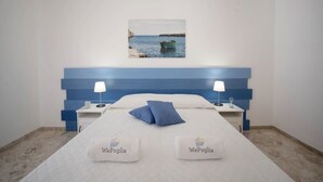 A hotel room with a bed, two bedside tables, a nightstand, a wall-mounted picture, and two pillows with the logo 'WePuglia'.