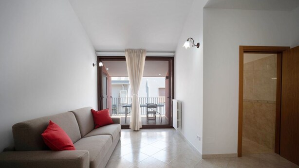 A modern living room with a sofa, a dining table, and a view to an outdoor balcony.