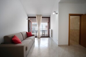 A modern living room with a sofa, a dining table, and a view to an outdoor balcony. - WePuglia – Dimora Melograno, house with priv.terrace&veranda, A/C, Wi-Fi (Polignano a Mare)