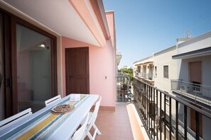 Een balkon met een tafel en stoelen, een deur en uitzicht op omliggende gebouwen.