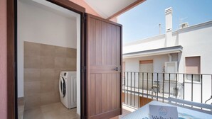 A balcony with a sign, a washing machine, and a door leading to a room.