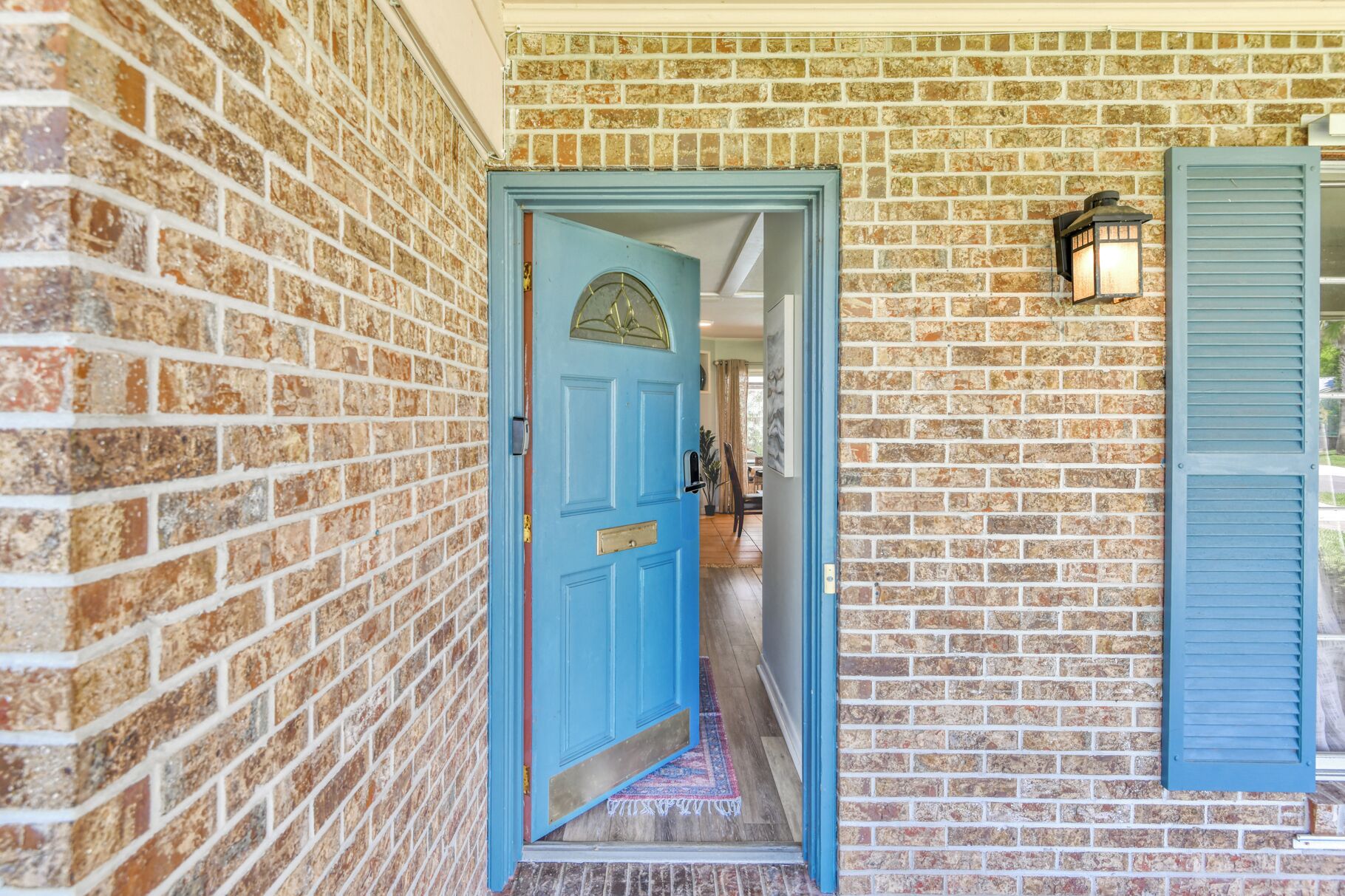 Fachada de tijolos com porta azul e um candeeiro fixado na parede.