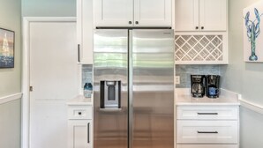 Una cocina con armarios blancos, un refrigerador de acero inoxidable, una cafetera y un hervidor.